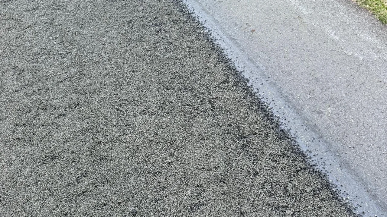 A dark bitumen spray seal surface beside a concrete kerb and grass