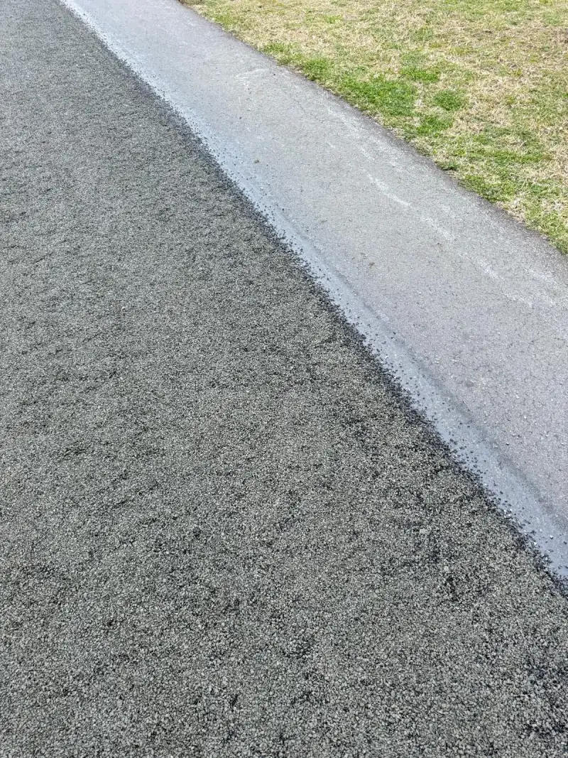 A newly laid asphalt driveway edge finished against a concrete path