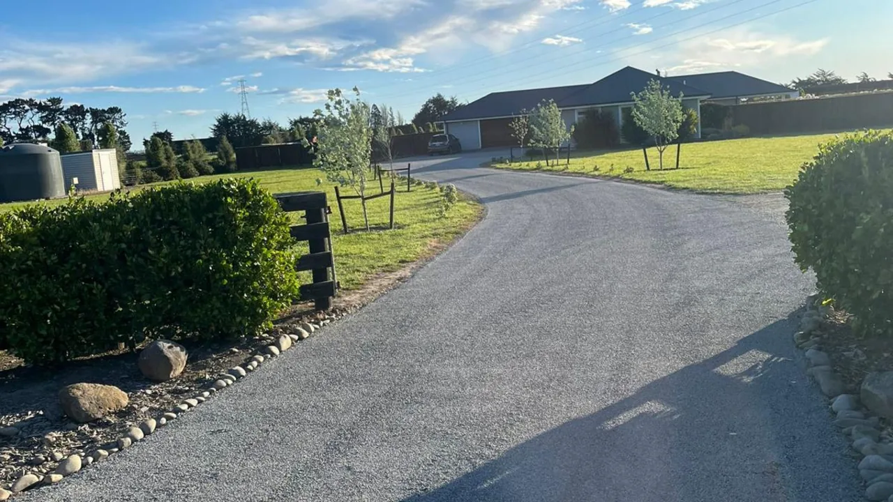 A sealed driveway curving through a rural property, with hedges, lawn and a single-storey house in the background