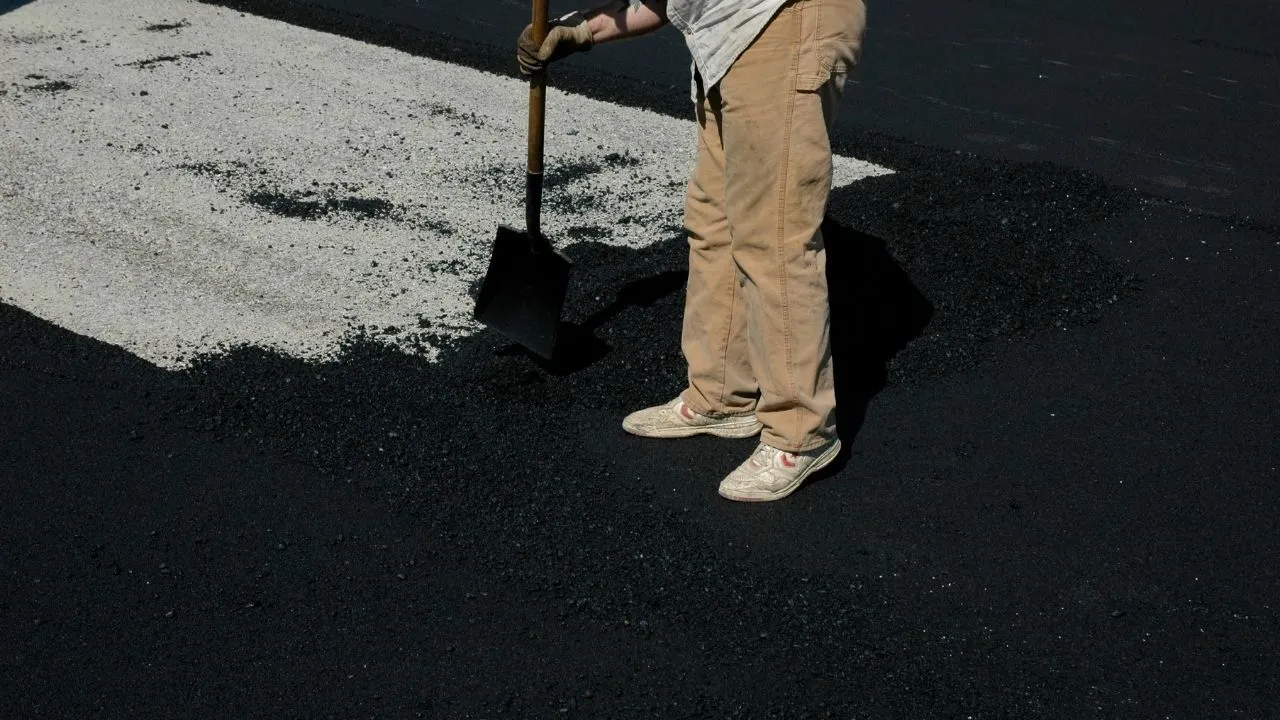A Road Ways worker spreading fresh asphalt over a prepared surface