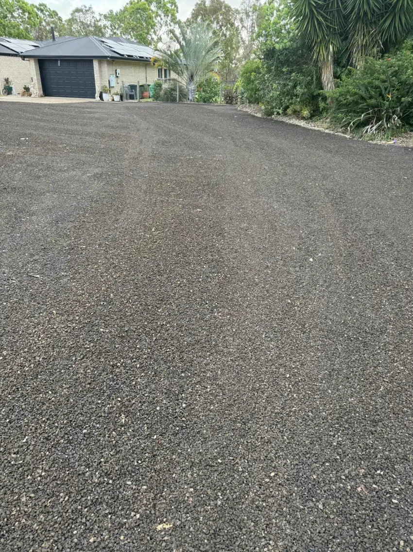 A newly sealed dark driveway leading up to a white brick home