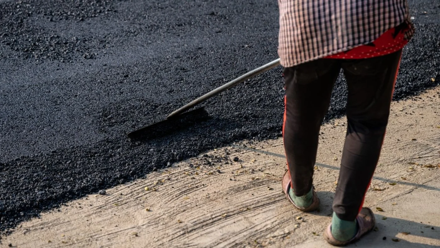 A Road Ways worker spreading hot mix asphalt across a prepared surface