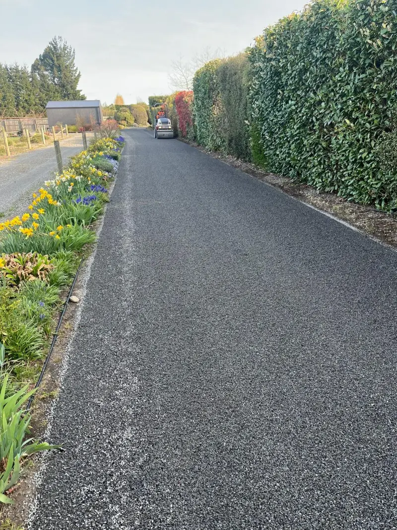 A long residential driveway edged with hedges and flowering garden beds